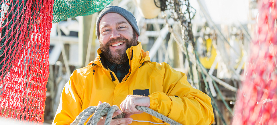 Smiling bearded fisherman coiling a line on the deck of a trawler